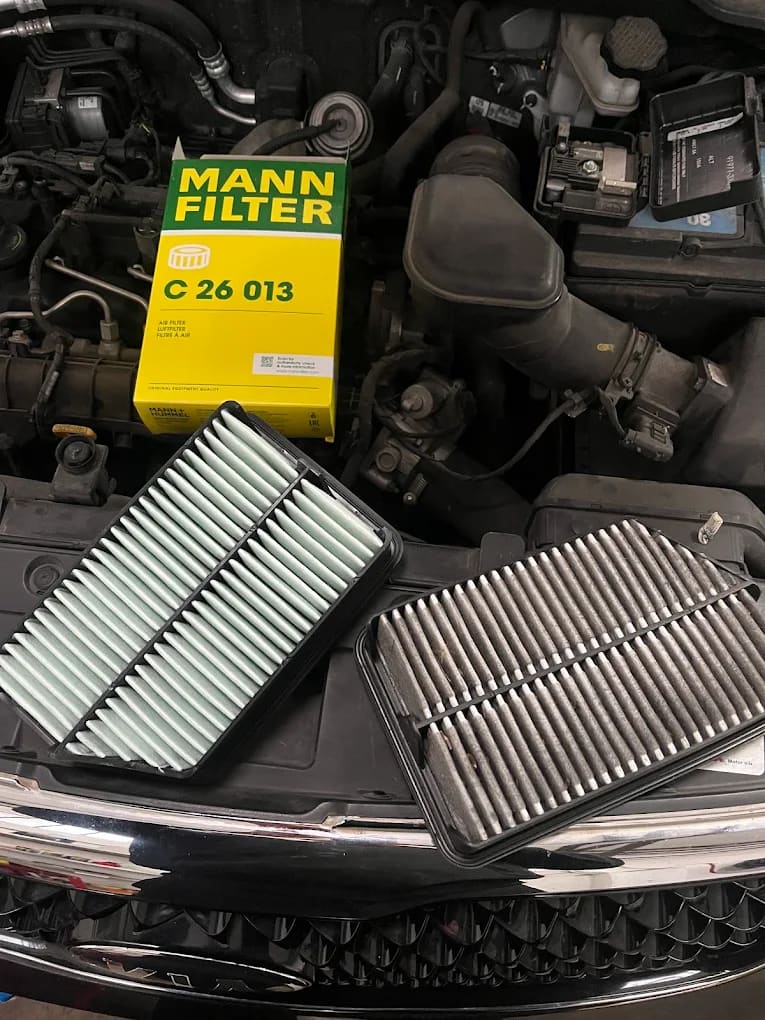 Filtre à air neuf à gauche et filtre à air usagé, gris et encrassé, à droite, posés sur le moteur devant la boîte du filtre neuf